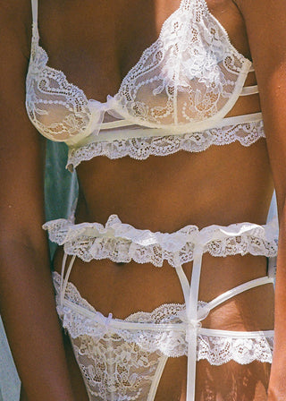 Woman wears a playful white garter belt with delicate lace all around your waist. It has bow details and makes the perfect wedding lingerie set. It’s from Lioa Lingerie, a Swiss Lingerie Brand.